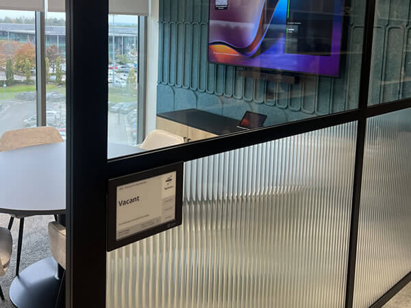 Joan Room Booking Panel showing “Vacant” status outside Synextra’s meeting room with view of Teams-enabled display inside.